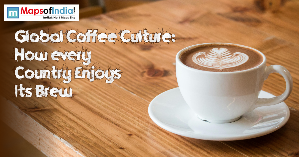 A cup of coffee placed on a brown table with a logo of maps of india on the left corner of the image