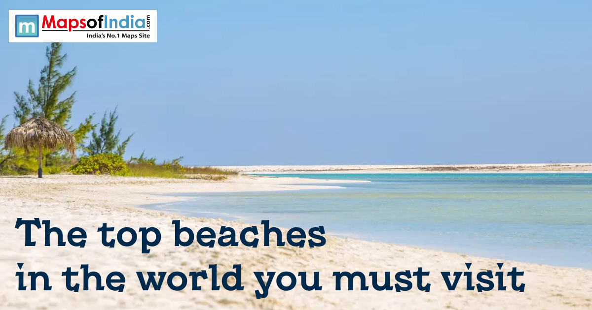 A serene tropical beach with white sand, turquoise water, and a thatched umbrella under a clear blue sky. The text "The top beaches in the world you must visit" is at the bottom, with a "MapsOfIndia" logo in the top left.