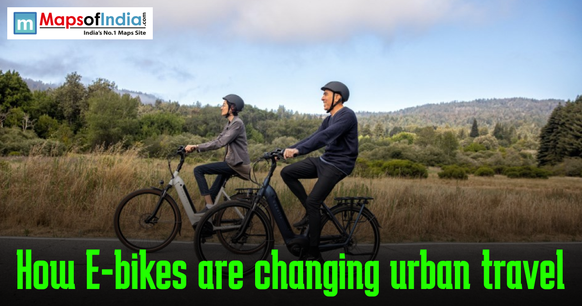 Two adults wearing helmets ride electric bikes along a scenic road with green hills in the background, with the text “How E-bikes are changing urban travel” and a Maps of India logo displayed