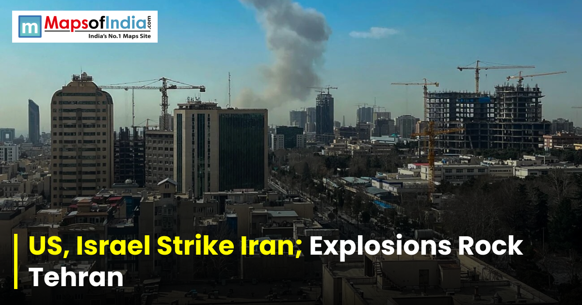 Smoke rising over Tehran’s skyline with high-rise buildings and construction cranes, overlaid with the headline “US, Israel Strike Iran, Explosions Rock Tehran” and a Maps of India logo